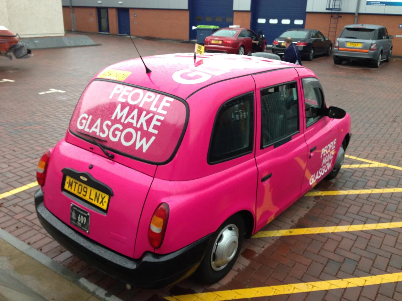"People Make Glasgow" pink city-campaign wrap on a Glasgow black-cab taxi, from Clyde Wraps' taxi advertising page.