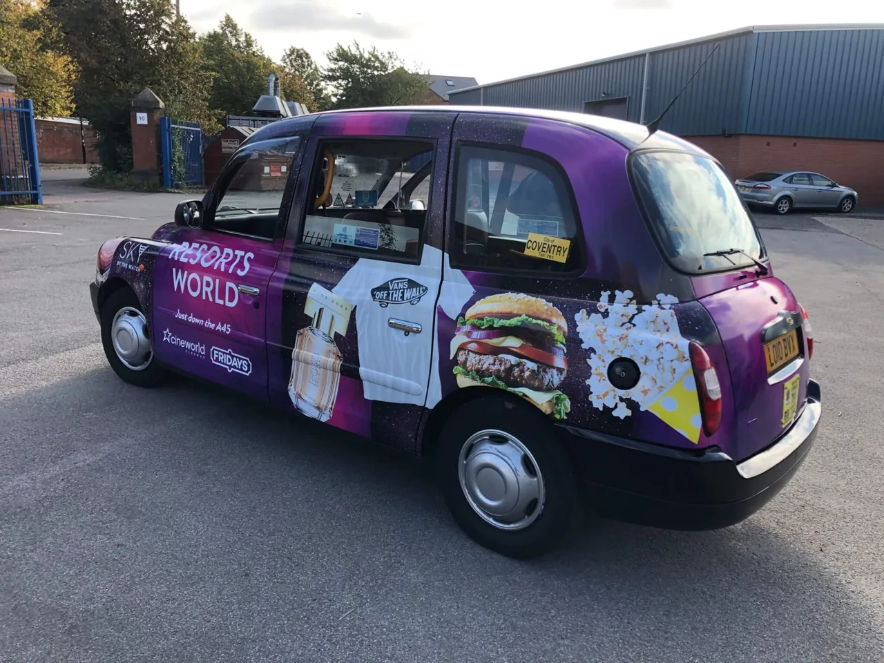 Full-wrapped London black-cab taxi (Resorts World / Coventry) in a purple burger-and-drink livery, photographed on-street