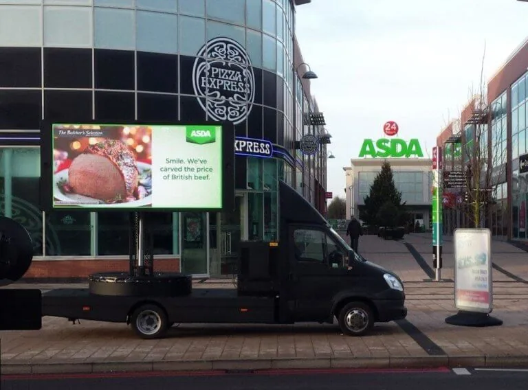 LED digital advertising van running an ASDA British-beef ad, parked at a retail park (Pizza Express / ASDA storefront behind)