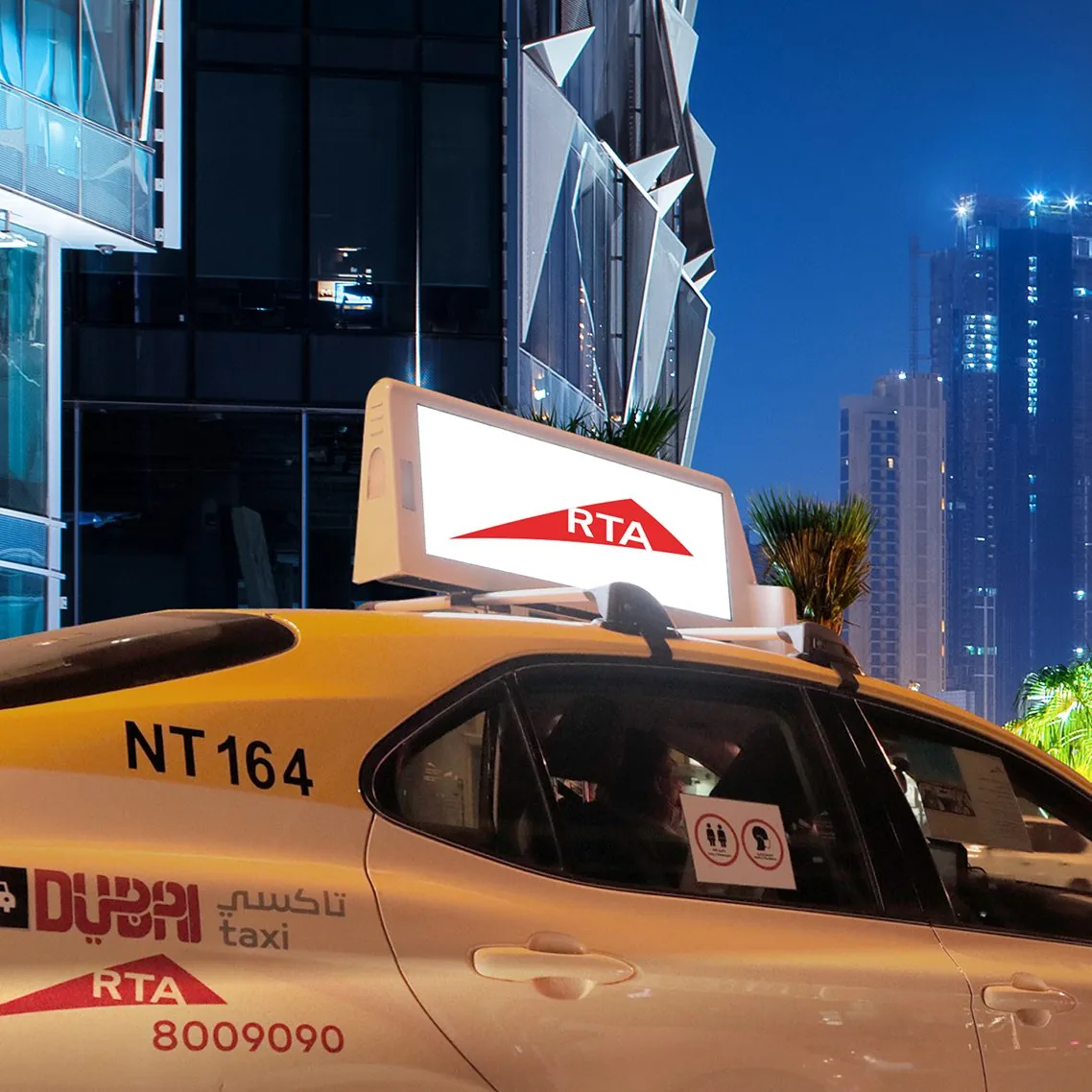 Dubai RTA taxi fitted with a digital rooftop screen (taxi-top DOOH), shot at night in Downtown Dubai
