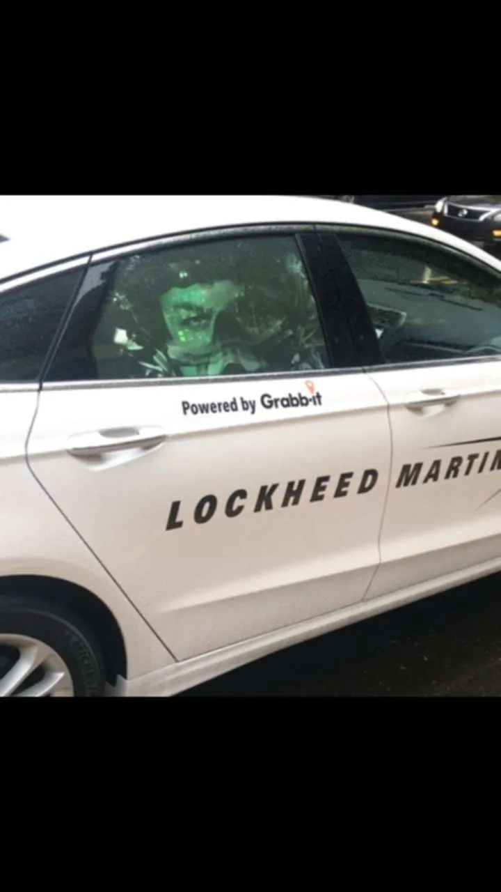 Lockheed Martin campaign on a Grabb-it rideshare car: 'Powered by Grabb-it' door decal with a Lockheed Martin brand wrap and a green digital ad on the rear side window (photo credited 'Provided By: Grabb-it').
