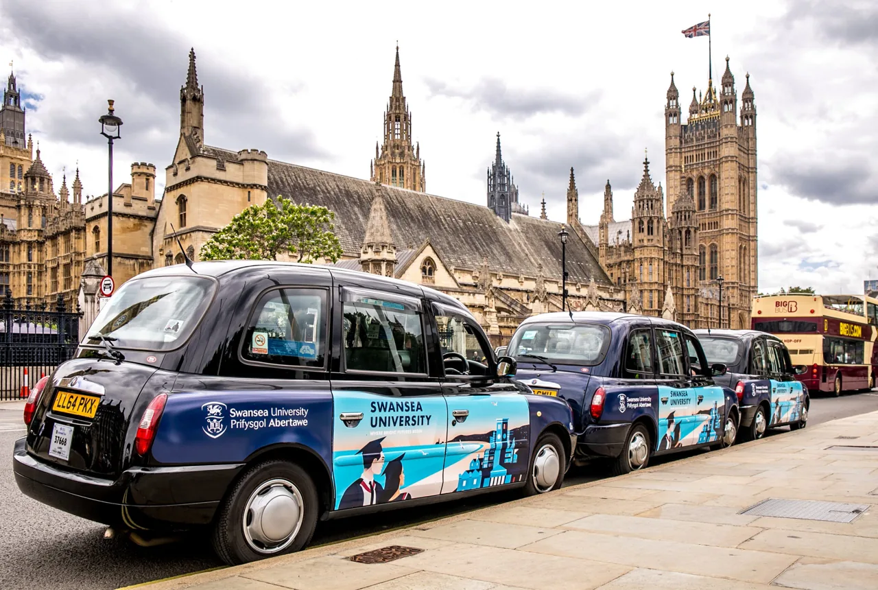 Swansea University full-livery taxi fleet lined up in front of the Houses of Parliament, Westminster (Huge Media own work)