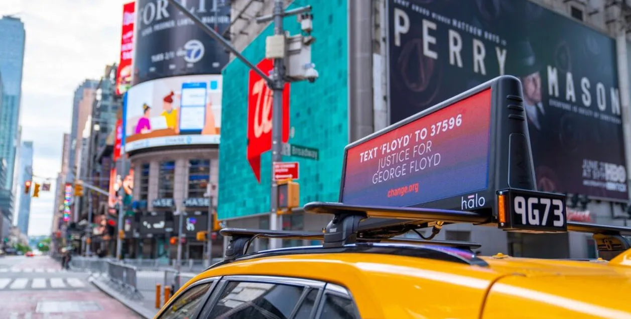 Lyft Media 'Halo' digital car-top screen mounted on a yellow NYC taxi in Times Square, running a change.org public-service message (2020).