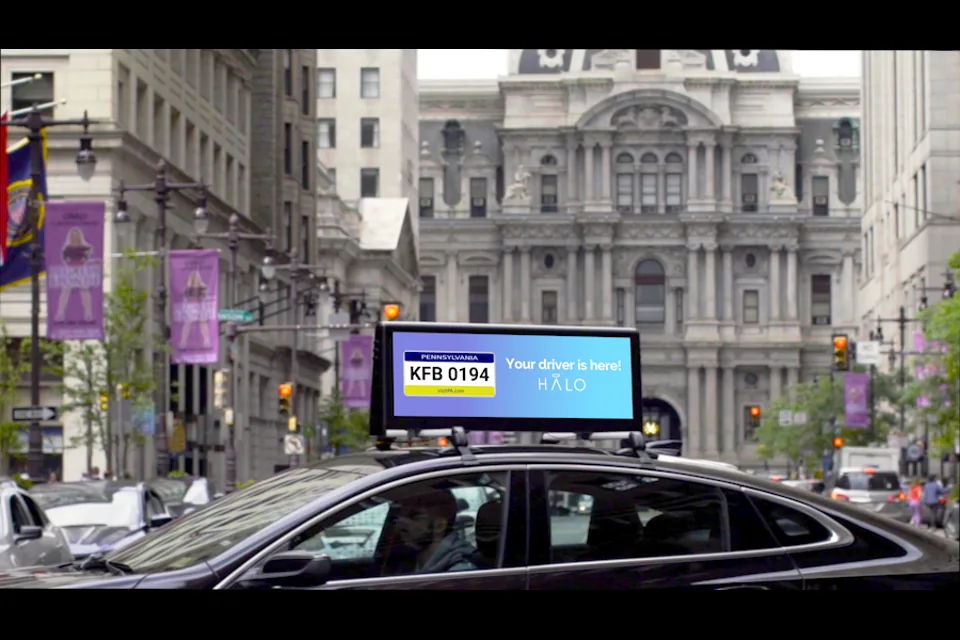 Halo car-top digital screen (Halo Cars, the roof-mounted network Lyft acquired to build Lyft Media) on a rideshare sedan in Philadelphia, showing the 'Your driver is here' license-plate display.