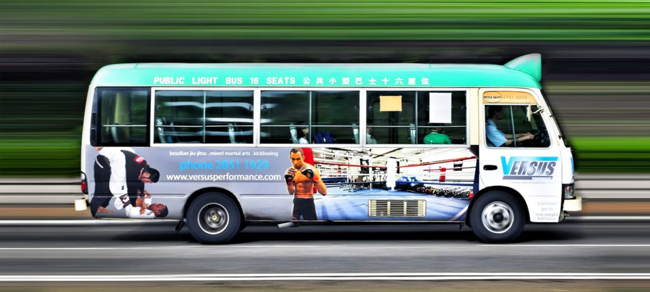 Hong Kong 16-seat green public light bus (minibus) wrapped for Versus Performance MMA gym; the vehicle carries a 'Media Savvy' operator decal