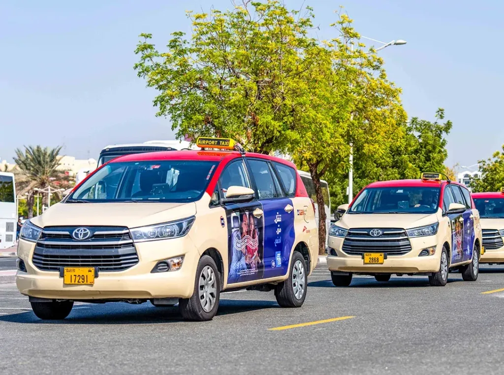 Dubai Airport Taxi (red-top Innova) with side-door American Express branding, Media247 transit-media fleet
