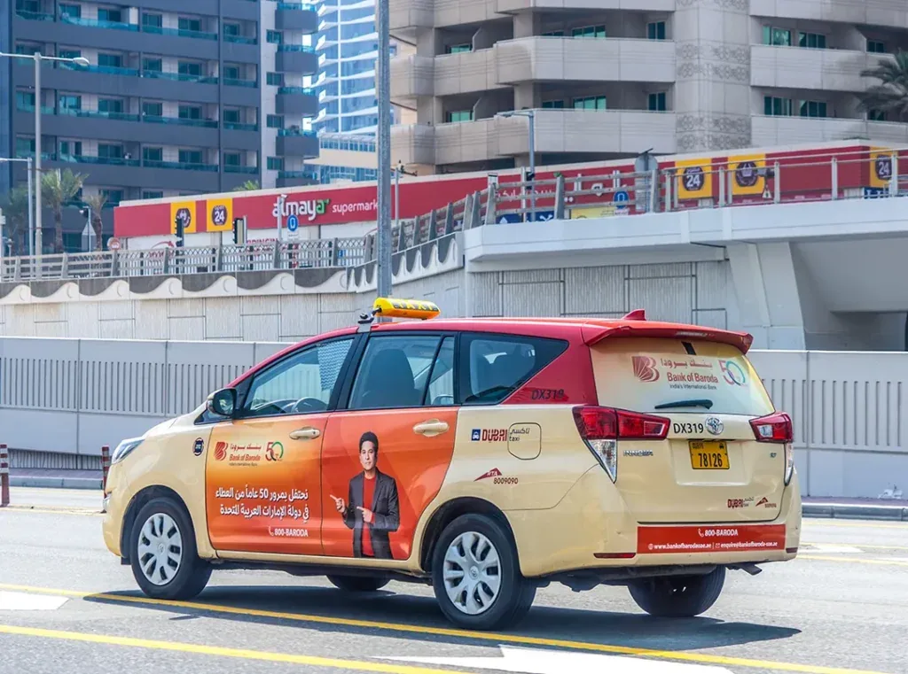 Full-body Bank of Baroda '50 years' wrap on a Dubai Taxi, photographed on a Dubai roadway
