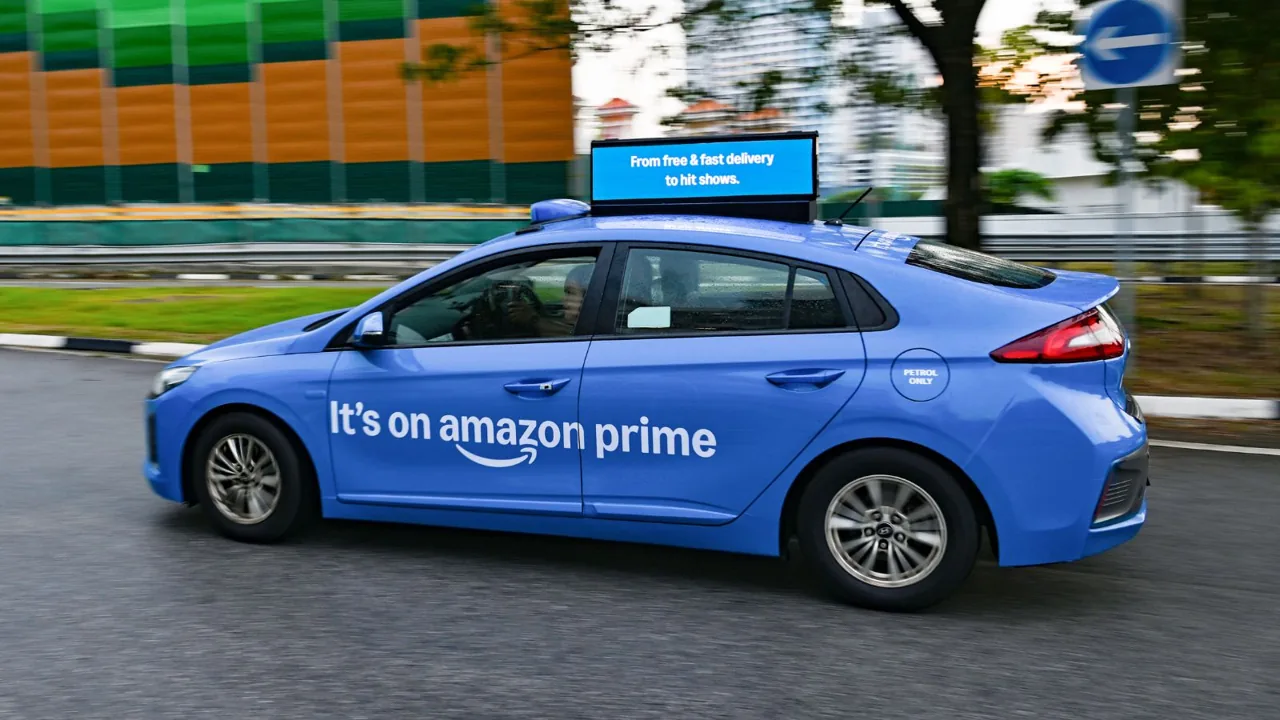 Amazon Prime full-side taxi wrap plus Moove Media smart digital taxi-top on a moving ComfortDelGro cab, Singapore — image from Marketing-Interactive trade coverage.
