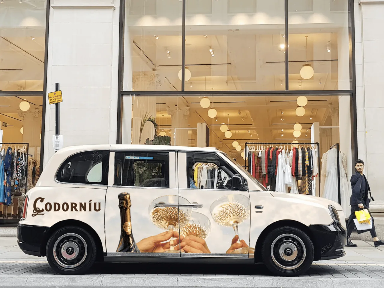 Codorniu sparkling wine full-body wrap on a London taxi outside a boutique storefront, One Day agency taxi advertising