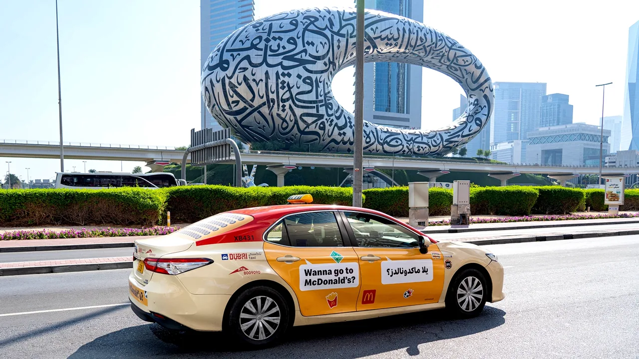 McDonald's full-taxi wrap driving along Sheikh Zayed Road past the Museum of the Future, Dubai