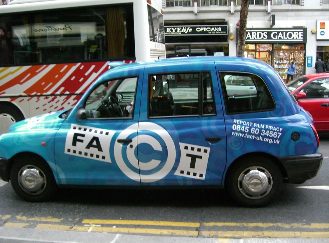 Full-livery wrapped London black cab for FACT 'Report Film Piracy' (fact-uk.org.uk) on a city street