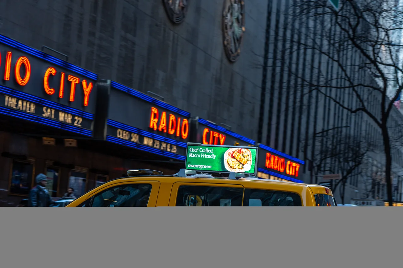 SOMO digital taxi-top on a NYC yellow cab passing Radio City Music Hall
