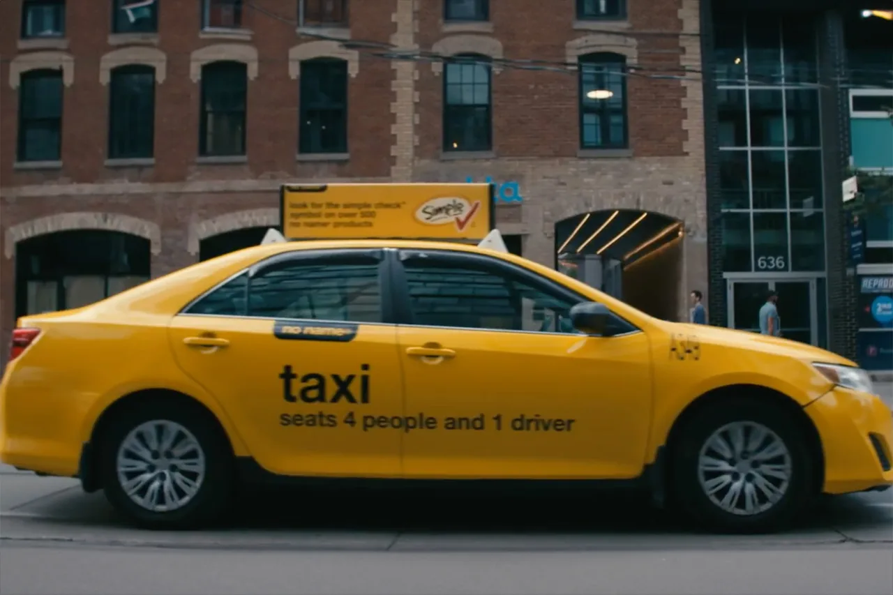 No Name 'taxi — seats 4 people and 1 driver' taxi-top sign plus door decals on a yellow cab (Statements Media)