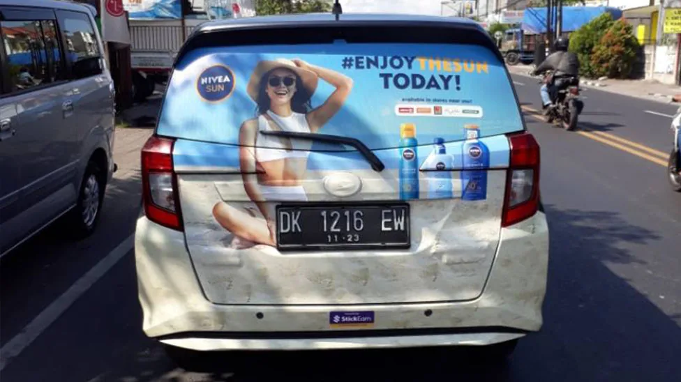 Nivea Sun 'Enjoy The Sun Today' rear-window car sticker branding (StickEarn StickMob), shot in street traffic with a StickEarn bumper decal — from StickEarn's own showcase gallery.