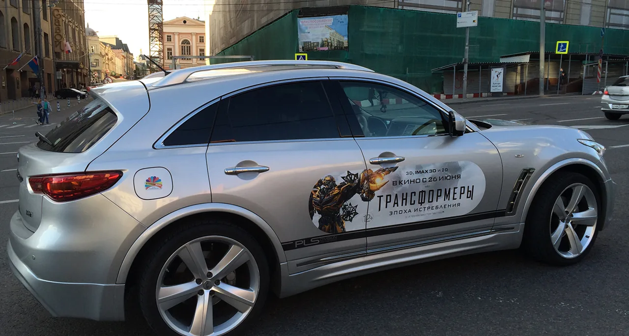 StickerRide mobile-billboard campaign for the film 'Transformers: Age of Extinction' - full side-door wrap on a silver Infiniti FX driving through Moscow.