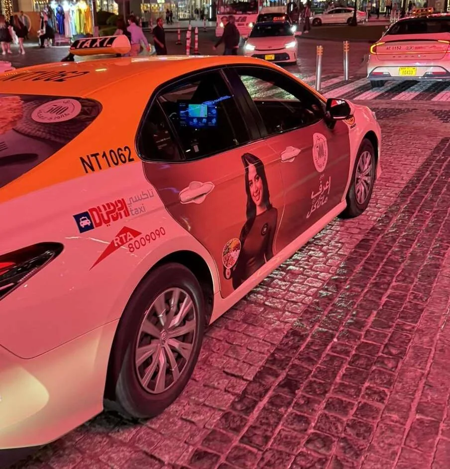 Dubai RTA taxi at night with an in-car interactive tablet screen mounted between the front seats (plus a side-door brand wrap) - the Binary/RTA in-taxi screen network Gen X Media resells