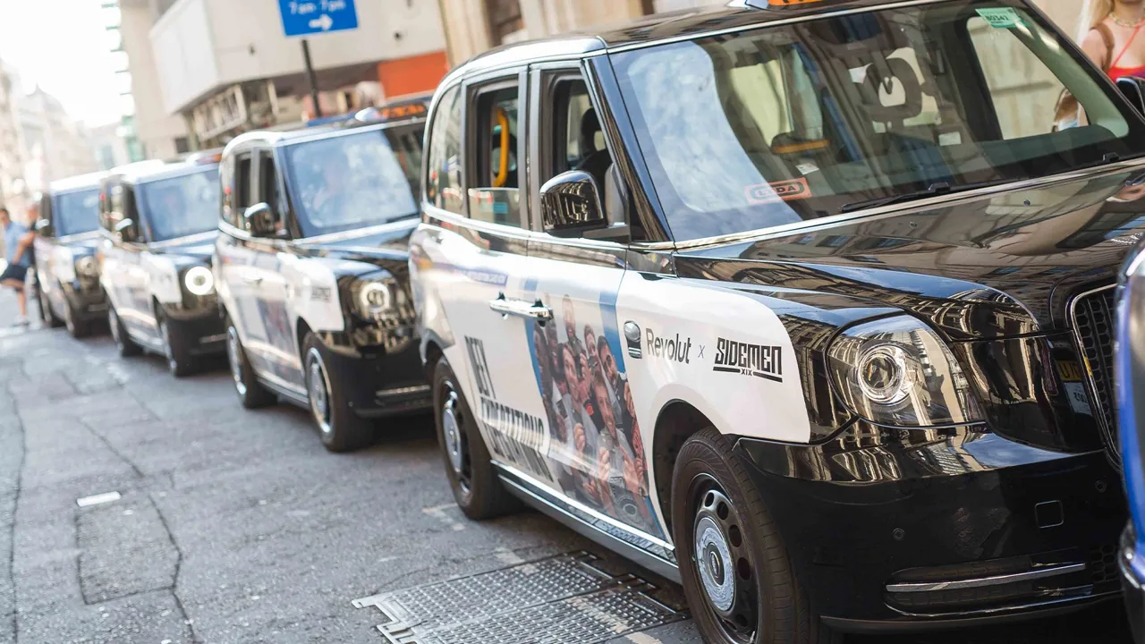 Line-up of branded black cabs with full-wrap taxi liveries on a London street (Transport Media taxi advertising gallery)