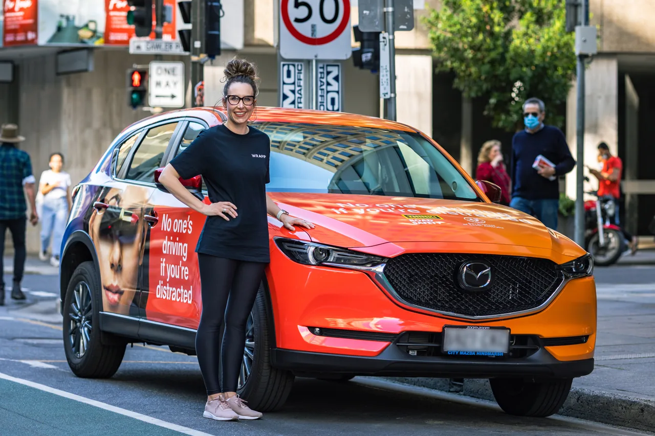 SAPOL / Towards Zero road-safety 'No one's driving if you're distracted' full wrap on an orange Mazda CX-5 on an Adelaide street, with Wrappr staff alongside