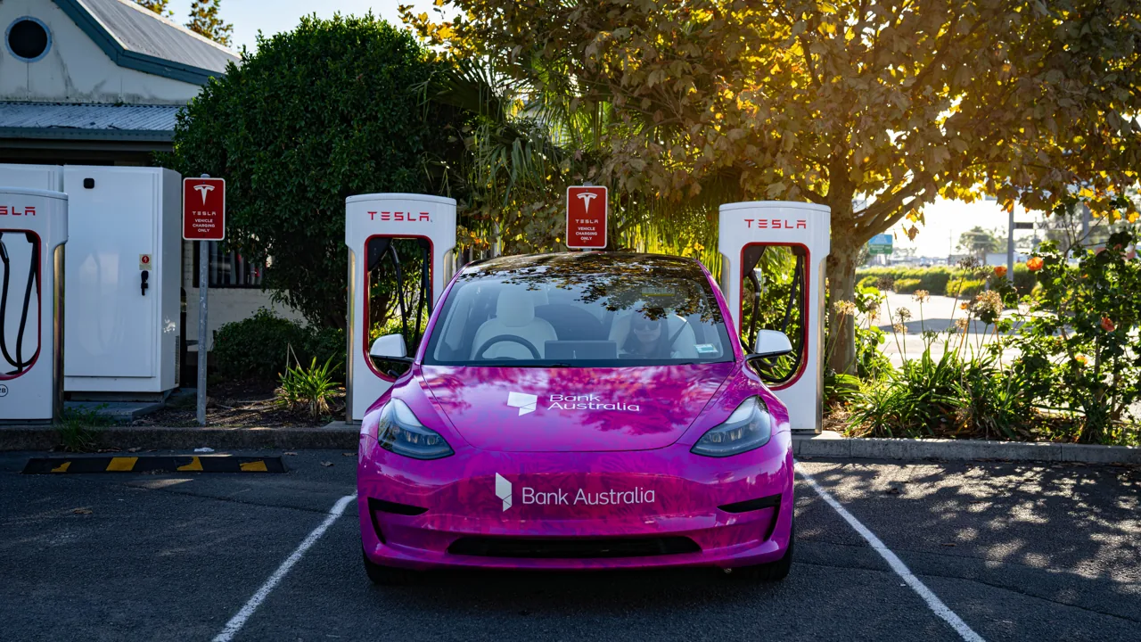 Bank Australia magenta full wrap on a Tesla Model 3 parked at a Tesla Supercharger station